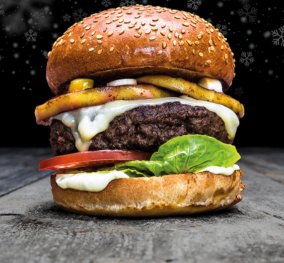 Burger in Sesambrötchen mit Rindfleisch Patty, gegrillten Apfelringen, Frühlingszwiebeln, Heumildkäse, Tomaten und Salat.